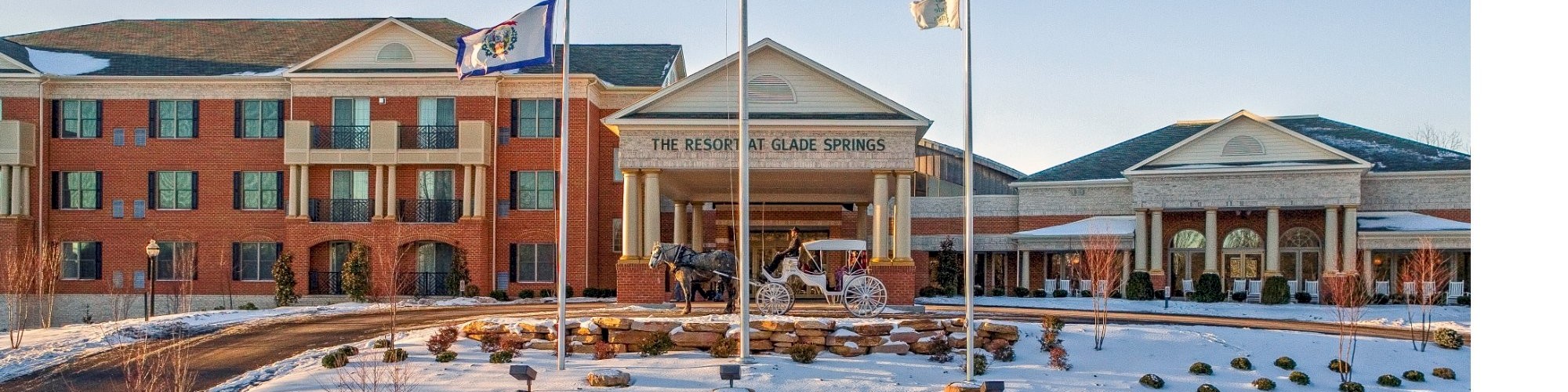 The image shows a large brick building with a snow-covered landscape, featuring a few flags and a circular driveway at the entrance.