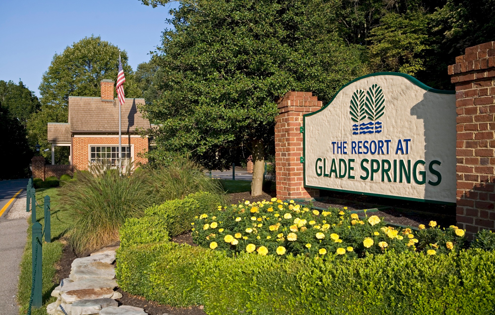 The image shows a sign for The Resort at Glade Springs, surrounded by greenery and yellow flowers in a landscaped area.