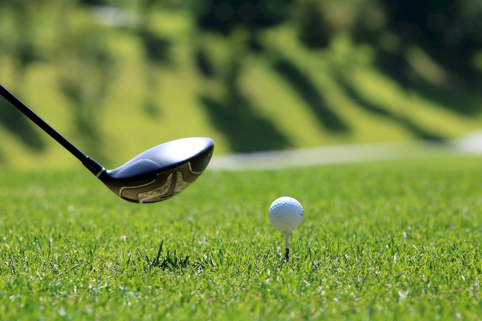 A golf club is about to hit a golf ball on a tee, set against a grassy background.