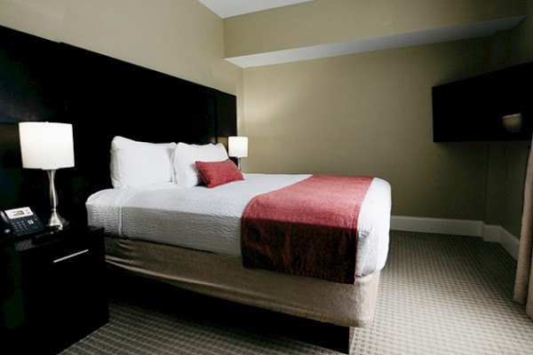 A neatly arranged hotel room features a large bed, two bedside lamps, a phone on the nightstand, and a TV mounted on the wall.