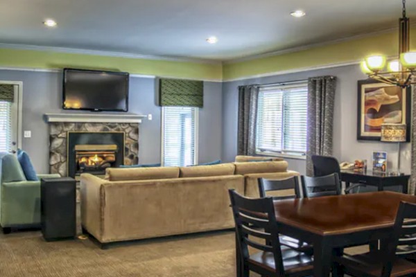 The image shows a modern living and dining area with a sofa, TV, fireplace, dining table, and overhead lighting.