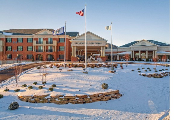 A building with flags flying, surrounded by snow and landscaping, featuring a central driveway and symmetrical architecture.