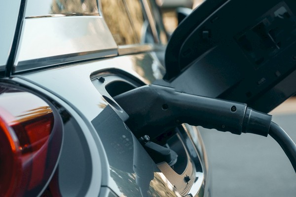 An electric vehicle is being charged, with the charging cable connected to the car's port near the rear taillight.