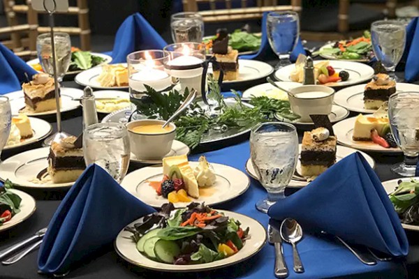 A set dining table features salads, desserts, and drinks with blue napkins and candles in the center.