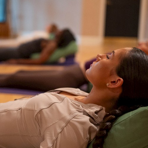 People lying on mats in a yoga or meditation class, relaxing with cushions in a serene room setting.