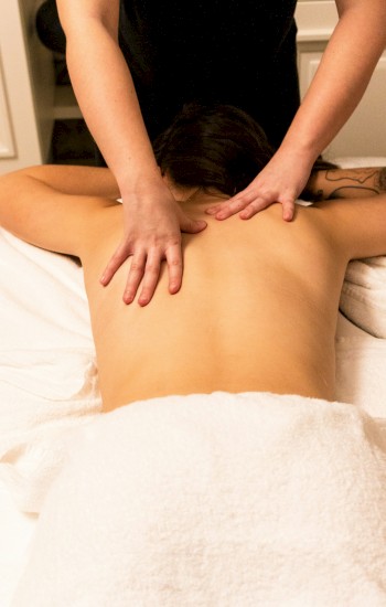 A person is receiving a back massage while lying on a table covered in a white towel.