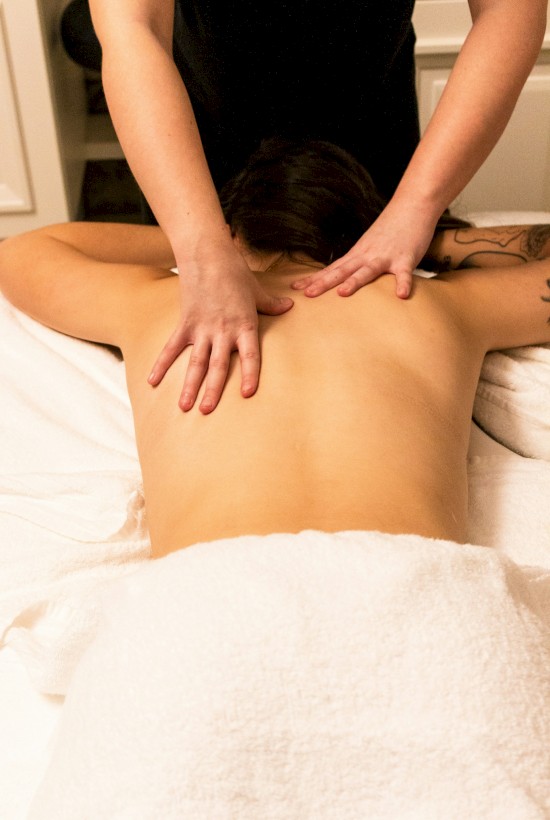 A person is receiving a back massage while lying on a table covered in a white towel.