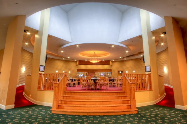 The image shows an elegant interior with a circular ceiling, wooden steps, and tables and chairs on a raised platform surrounded by soft lighting.