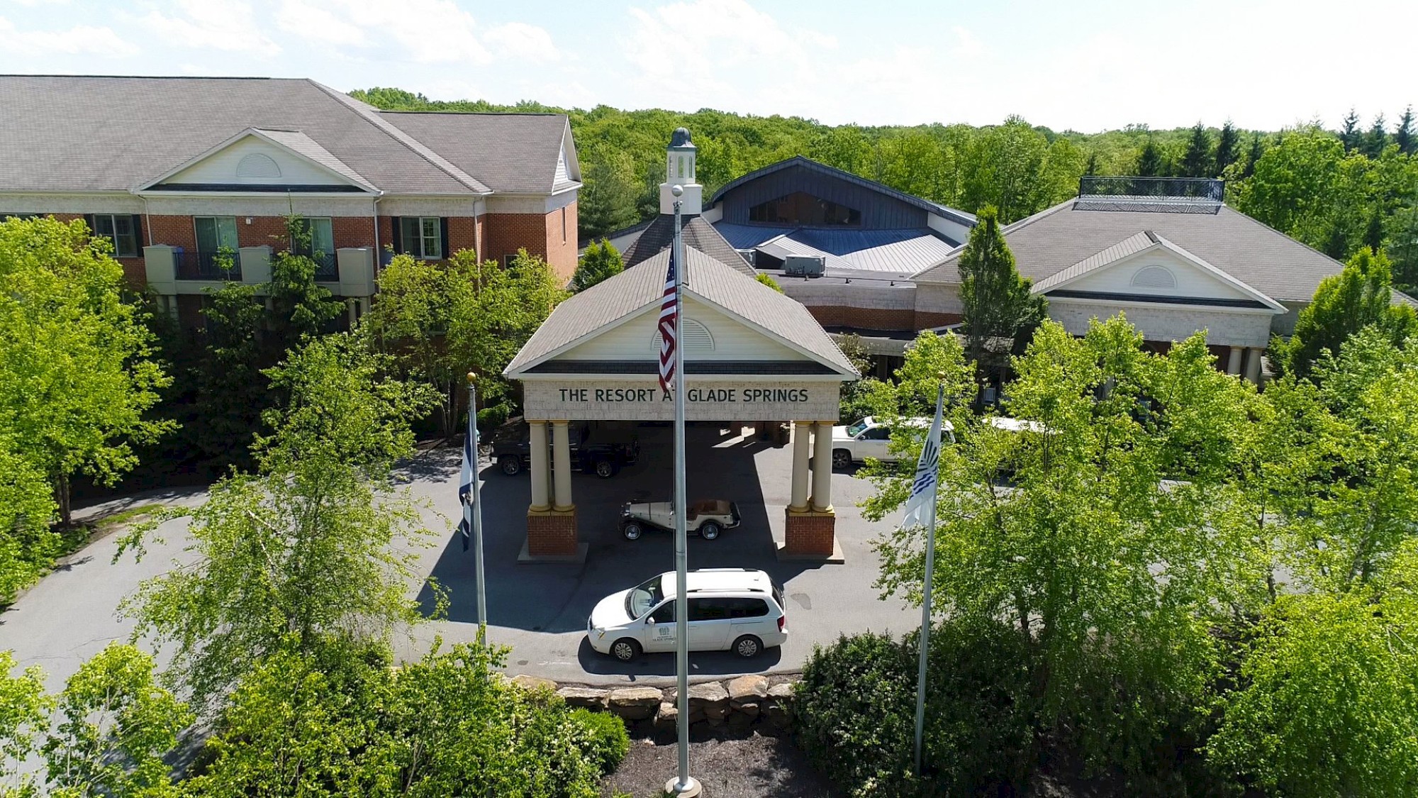 The image shows a resort entry with a sign, surrounded by greenery, featuring buildings, a driveway, and an American flag.