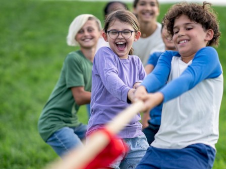 Kids are playing tug-of-war outdoors on a grassy field, looking happy and engaged in a fun activity with teamwork.