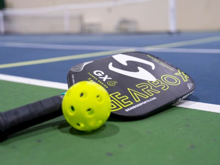 A pickleball paddle and yellow ball are on a court, ready for play.