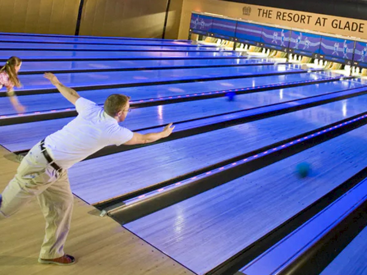 Two people are bowling at The Resort at Glade Springs, focusing on their game in a brightly lit bowling alley.