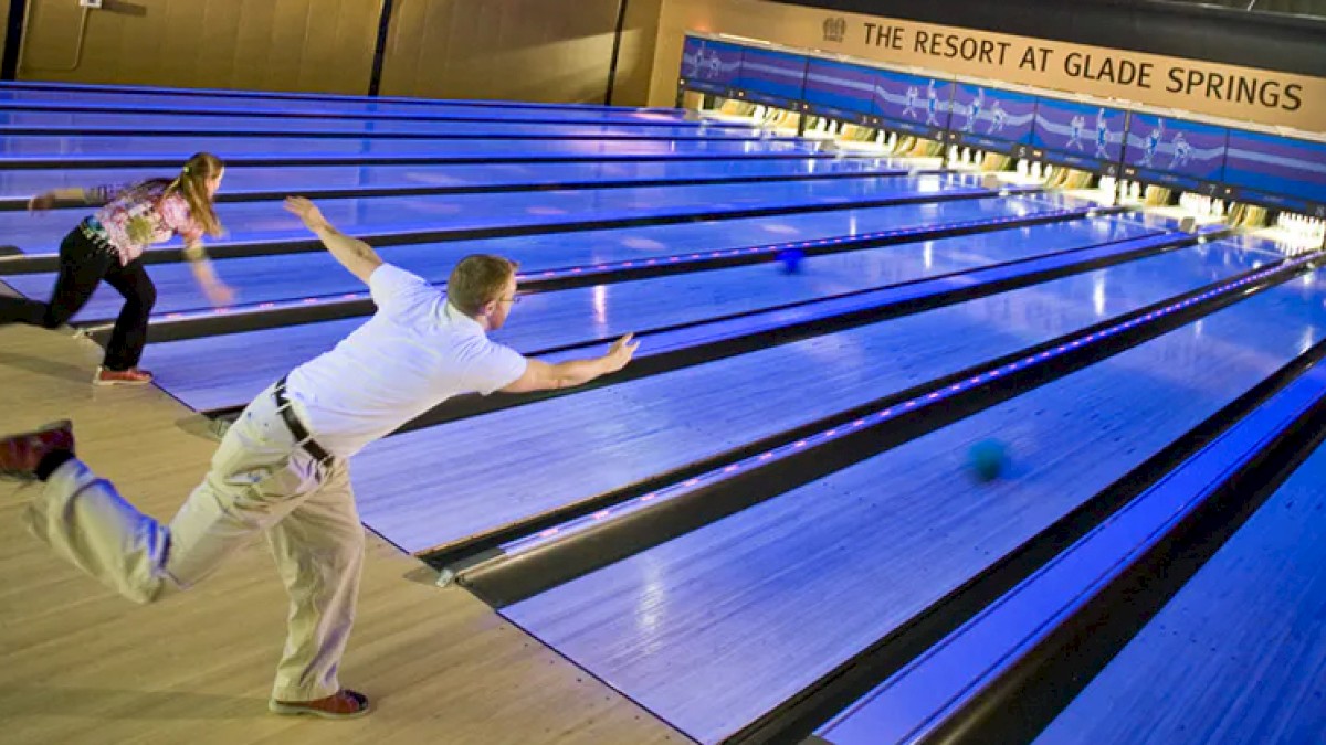 Two people are bowling at The Resort at Glade Springs, focusing on their game in a brightly lit bowling alley.