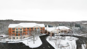 A building with a snow-covered landscape and trees in a winter setting. A road curves around, leading toward the entrance of the structure.