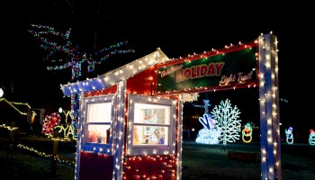 A festive holiday light display with colorful decorations, including trees and snowmen, surrounding a small booth illuminated at night.