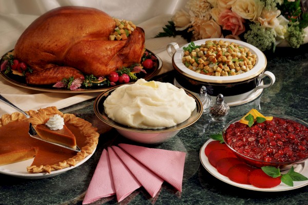 A Thanksgiving feast with roast turkey, stuffing, mashed potatoes, cranberry salad, and pumpkin pie, decorated with flowers and napkins.