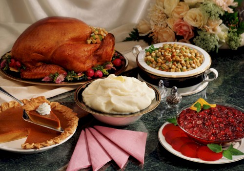 A Thanksgiving meal with roast turkey, stuffing, mashed potatoes, cranberry sauce, and pumpkin pie, set on a table with pink napkins.