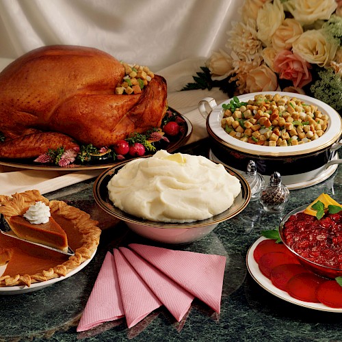 A Thanksgiving meal with roast turkey, stuffing, mashed potatoes, cranberry sauce, and pumpkin pie, set on a table with pink napkins.