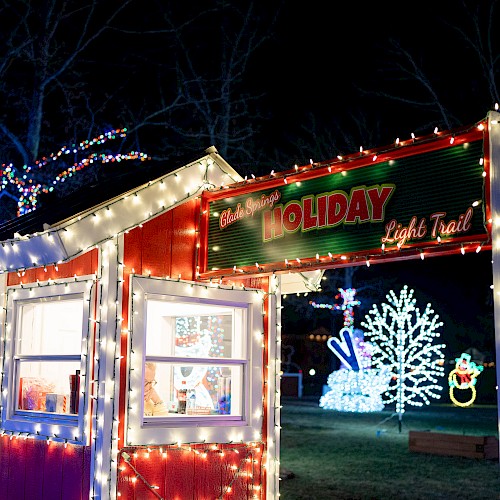 Festive holiday light trail featuring a decorated booth and vibrant Christmas light displays, including snowmen and trees, amidst a nighttime scene.