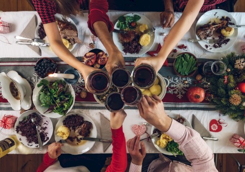 A festive table setting with plates of food, salads, and holiday decor. People raise glasses in a toast, celebrating together.