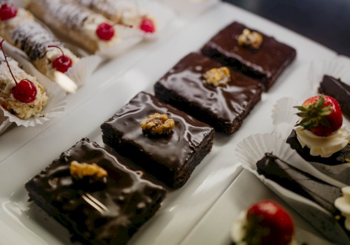 The image shows a selection of pastries on a platter, including chocolate brownies with walnuts, chocolate cakes with strawberries, and cannoli.