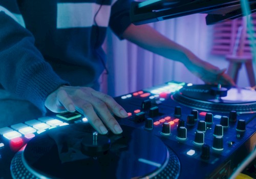 A DJ is mixing music on a console with glowing lights and controls in a dimly lit room, creating an energetic atmosphere.