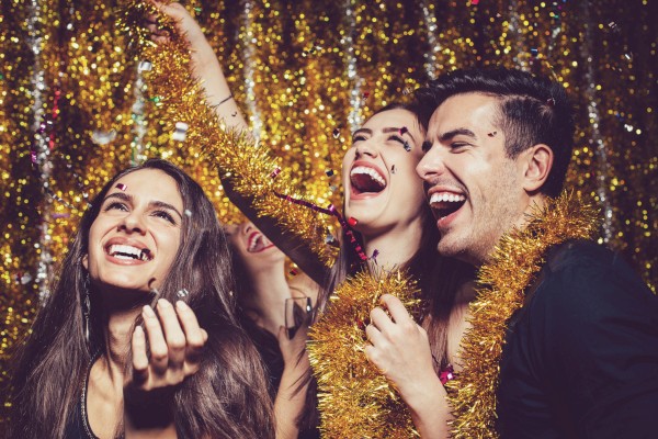 A group of people are celebrating, surrounded by glittering decorations and wearing tinsel, all smiling and enjoying the moment.