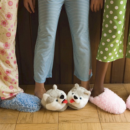 Three people wearing colorful pajamas and fluffy slippers stand on a wooden floor.