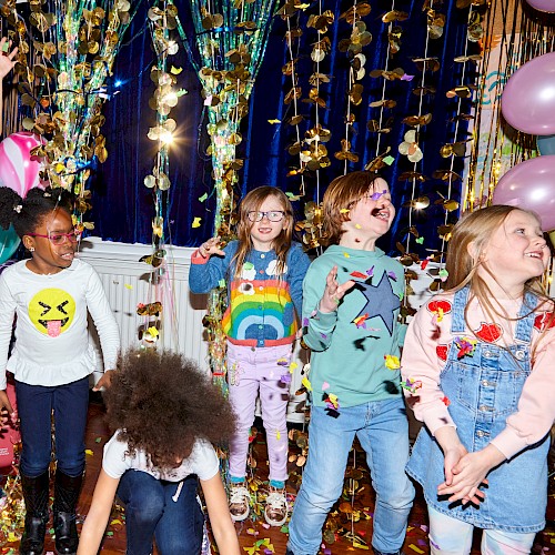 A group of children joyfully playing amid colorful balloons and decorations, with confetti in the air, creating a festive atmosphere.