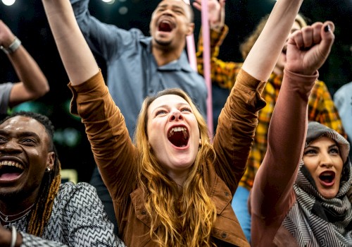 A diverse group of people are cheering energetically with their arms raised in a celebratory atmosphere.