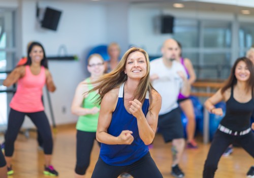 A group of people energetically participating in a dance workout class in a gym setting, all dressed in athletic wear.