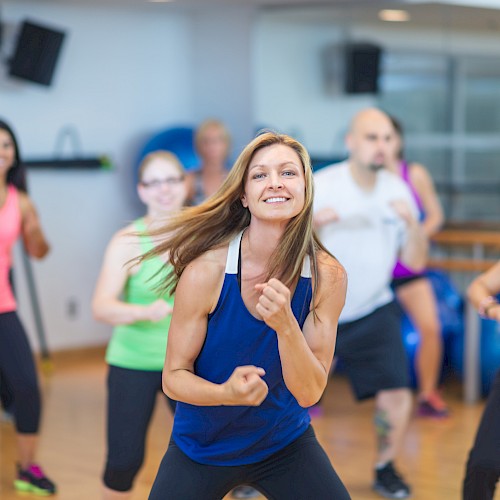 A group of people energetically participating in a dance workout class in a gym setting, all dressed in athletic wear.