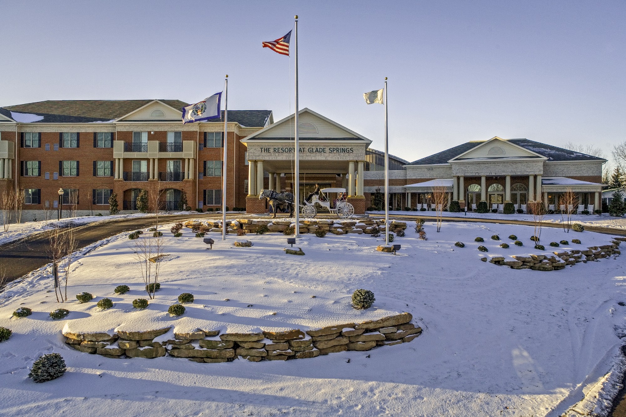 The image shows a large brick building with flags, snow-covered ground, landscaping, and a circular driveway, likely a hotel or resort.