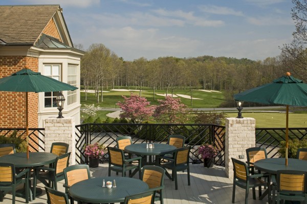 Outdoor patio with green umbrellas and tables, overlooking a golf course and trees on a clear day.