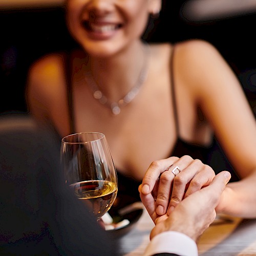 A couple holds hands across a table with wine and lit candles, suggesting a romantic setting.